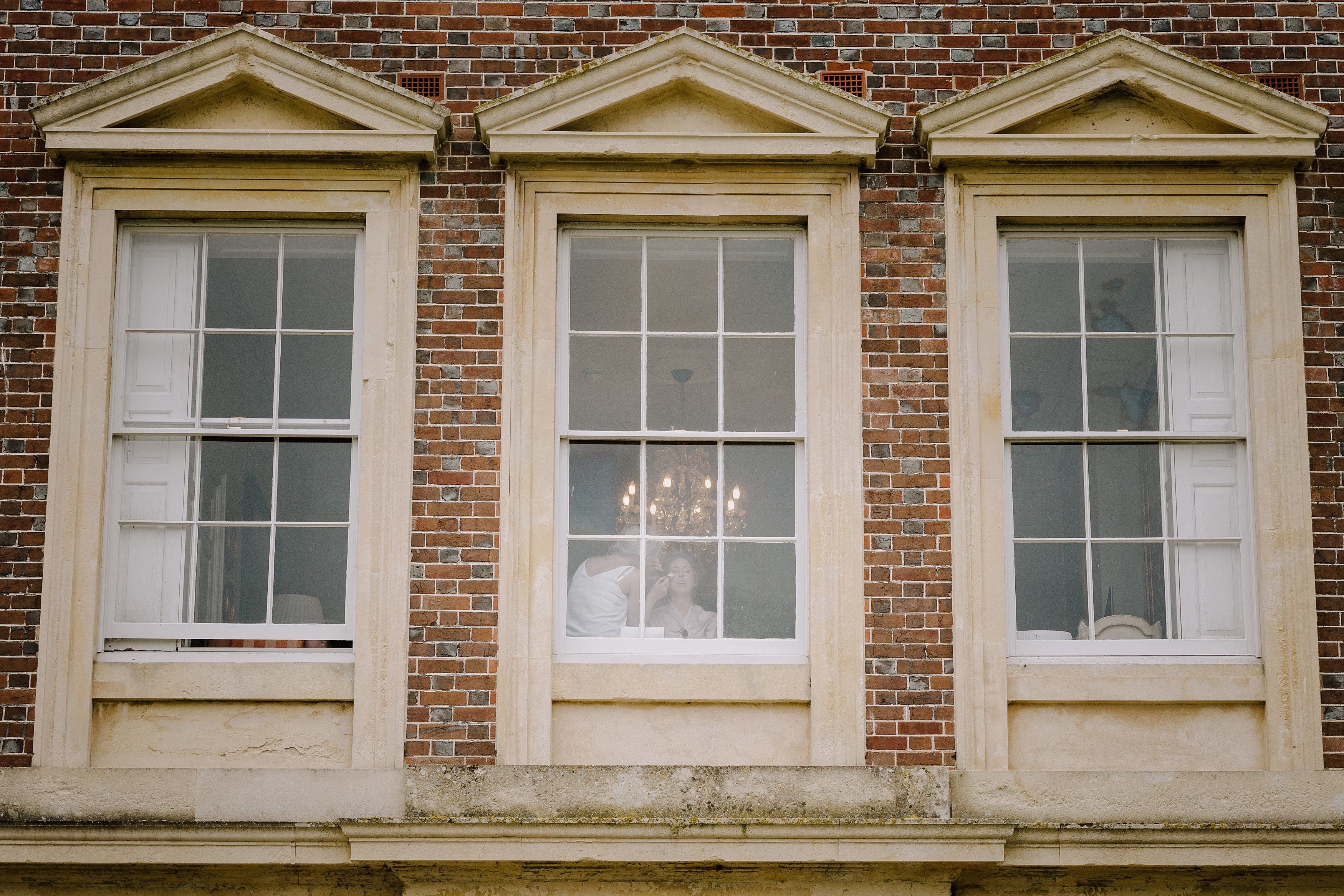 A view through the window showing a bride have her make up done