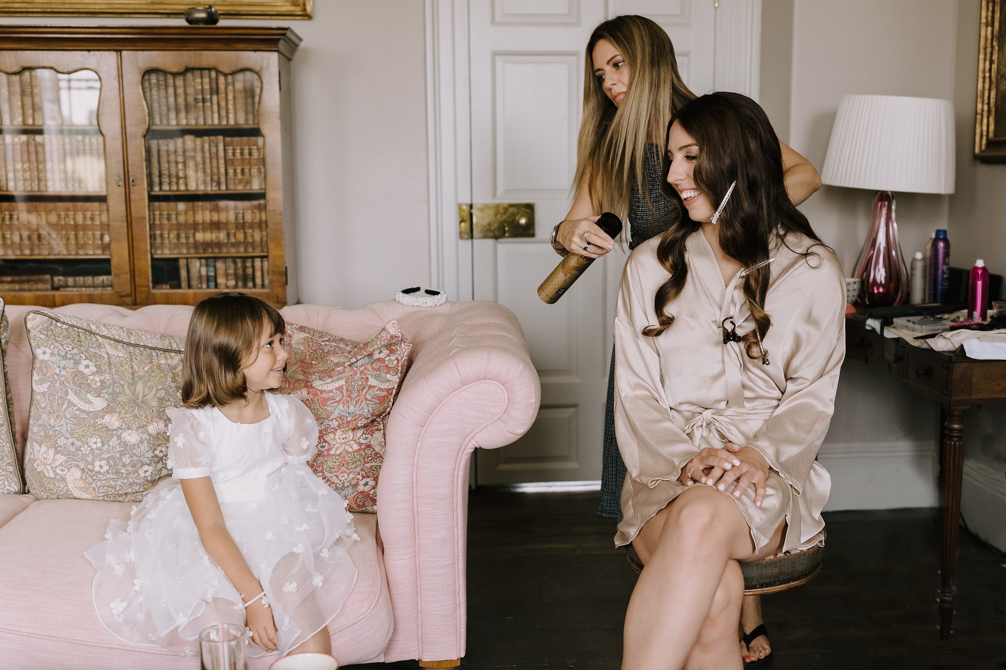 A bride having her hair done next to her flower girl