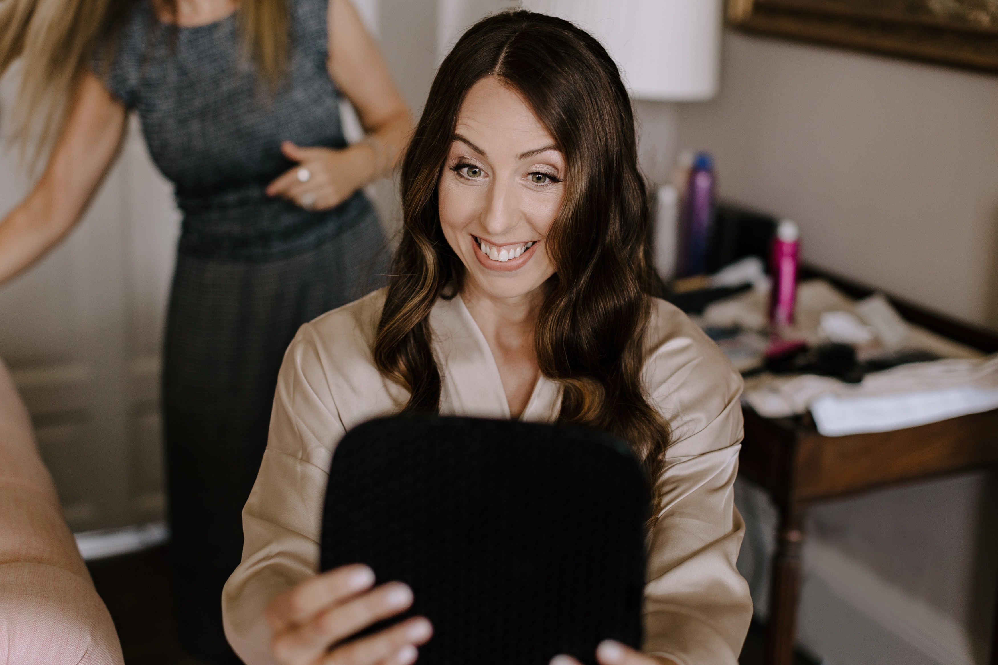 A bride looking pleased with her wedding day hair as she looks in the mirror