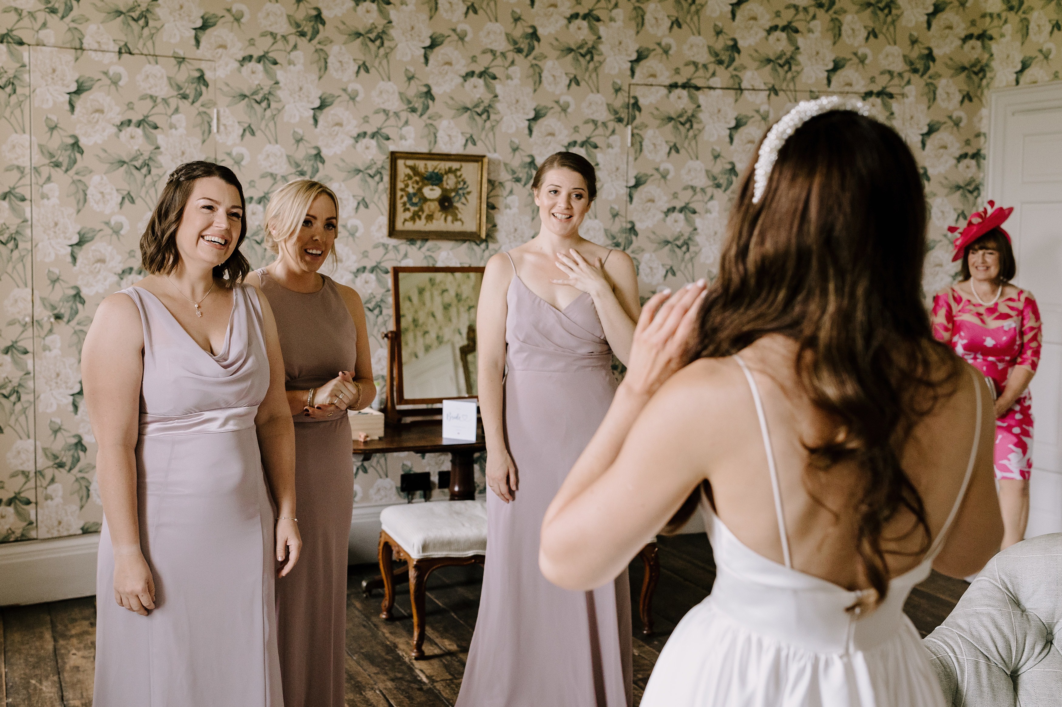 Bride showing her bridesmaids and mother of the bride her wedding day look for the first time