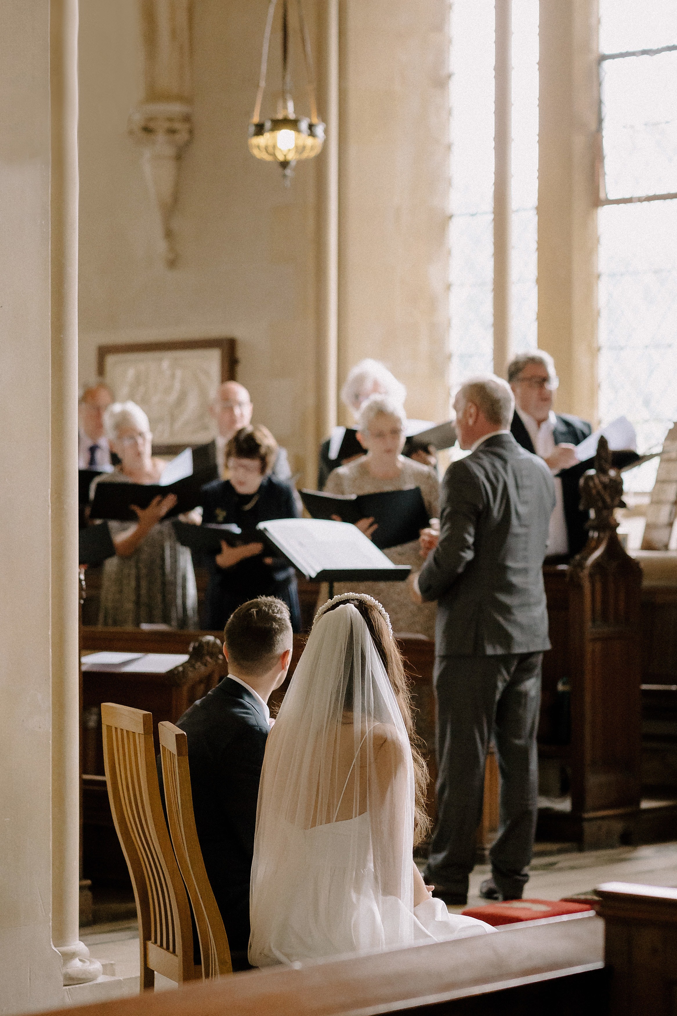 Bride and groom in foreground looking away from the camera at the choir singing