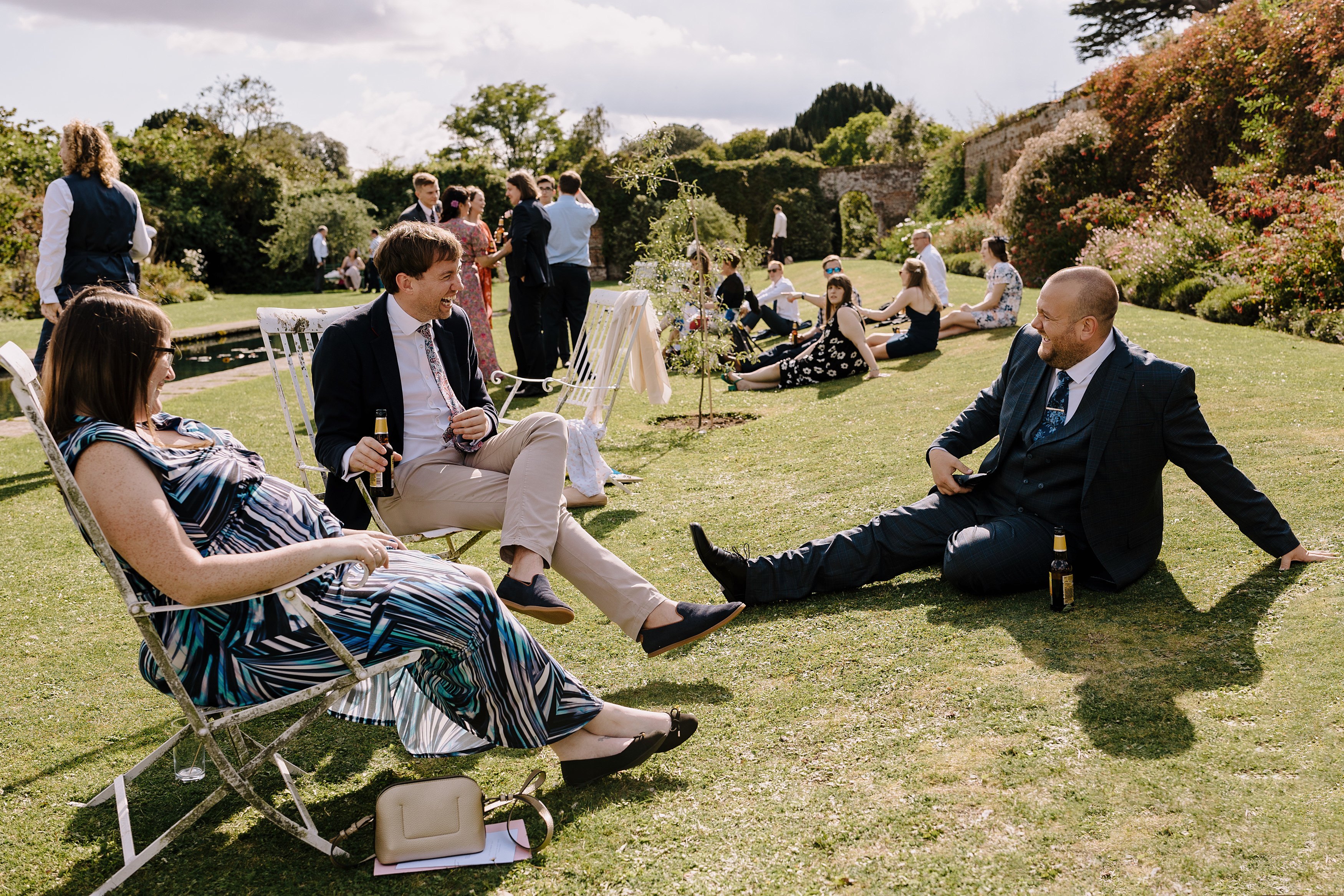 Wedding guests sit on the grass and enjoy drinks in the walled garden at Goodnestone Park