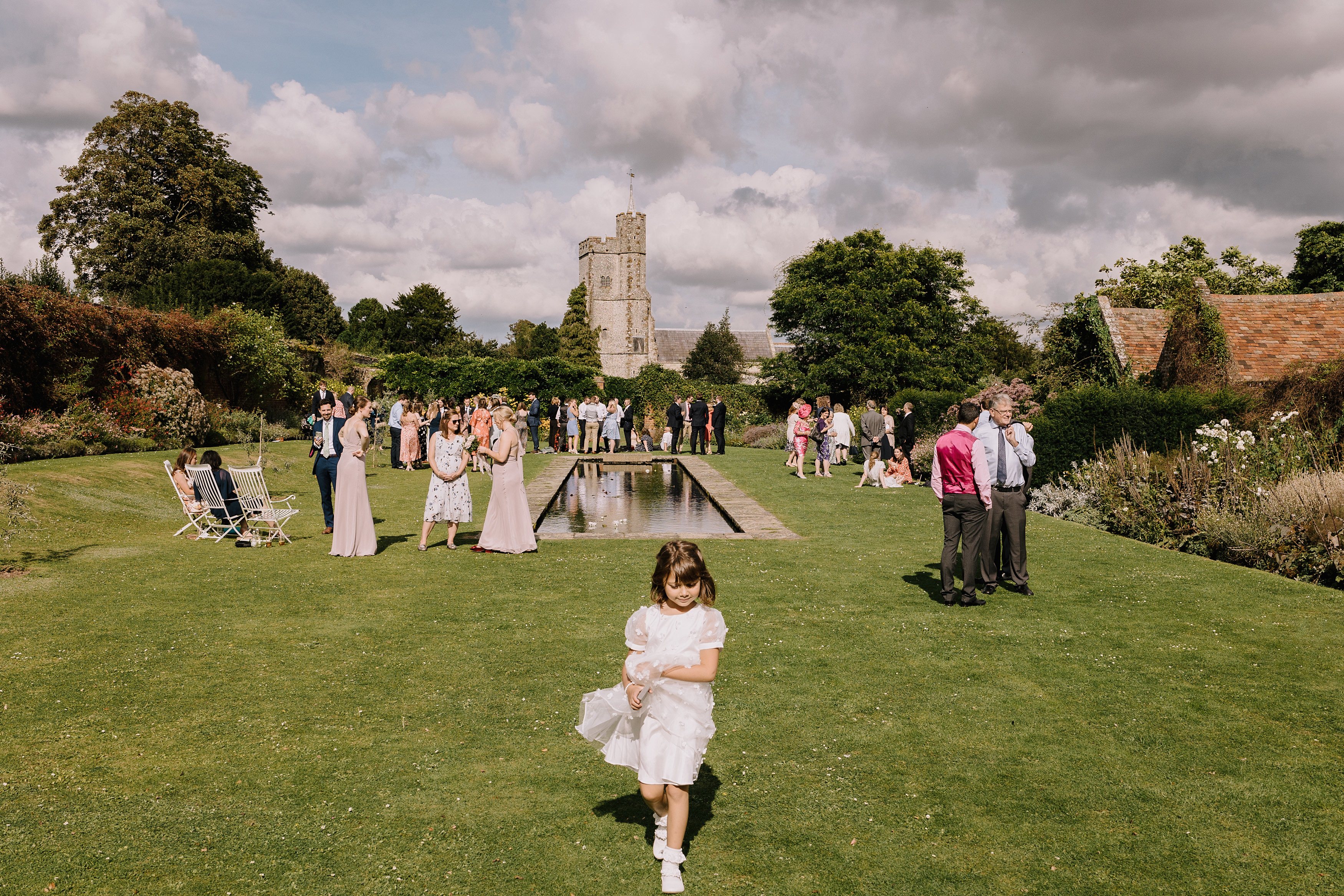 A photo of all the wedding guests with flower girl in the foreground and the Church of Holy Cross in the background