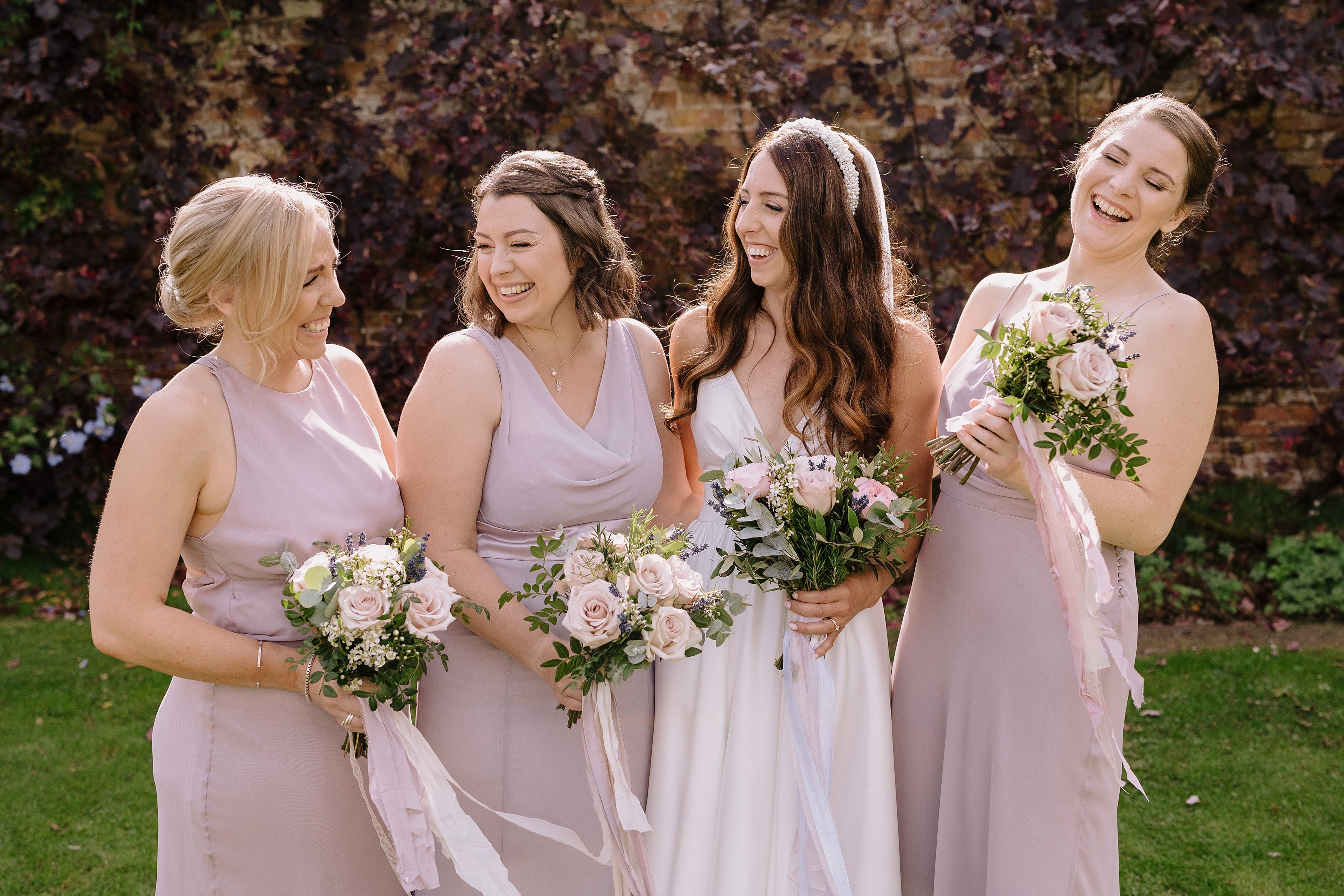 A bride laughing with her bridesmaids, all holding bouquets