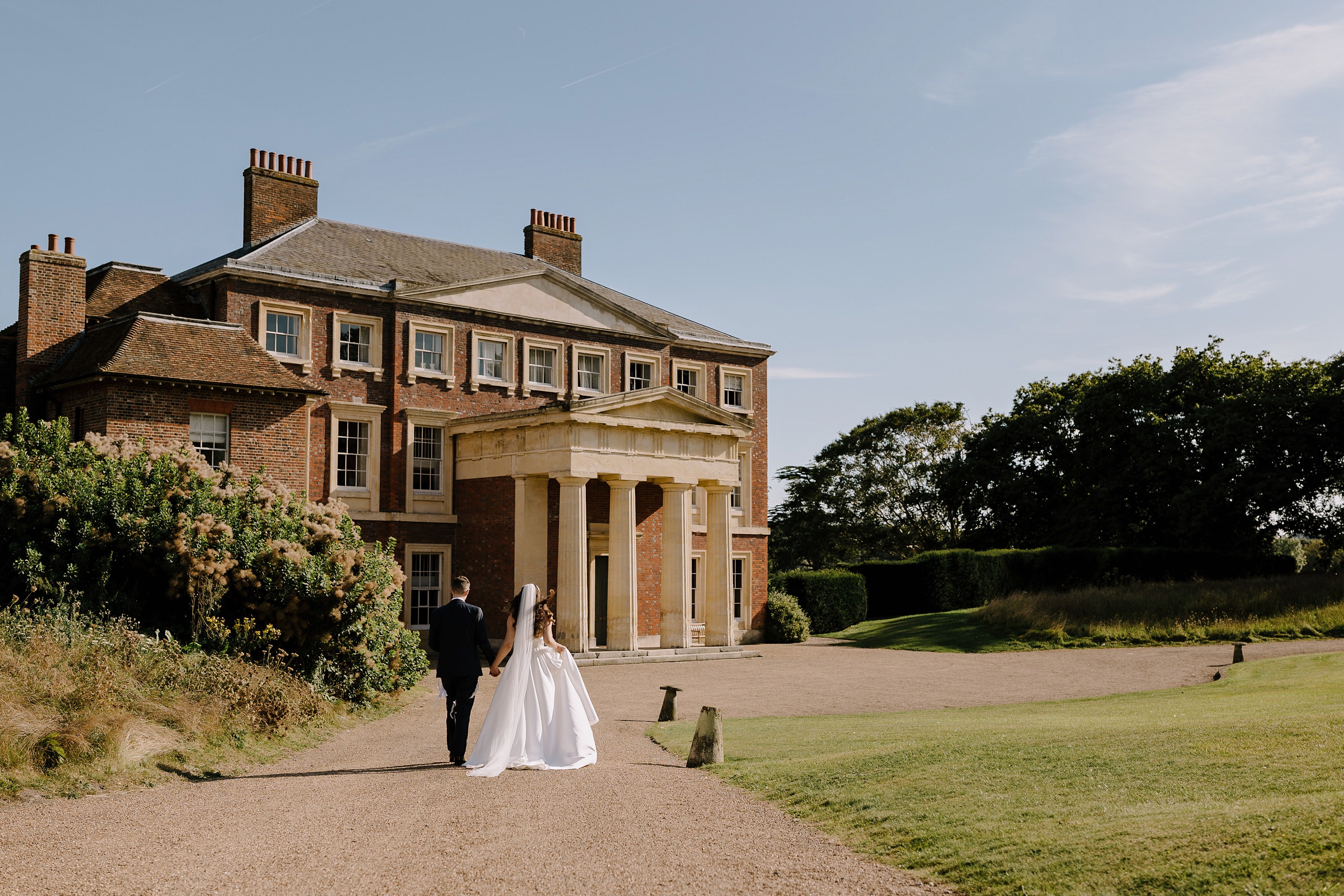 Bride and groom walking towards Goodnestone House hand in hand