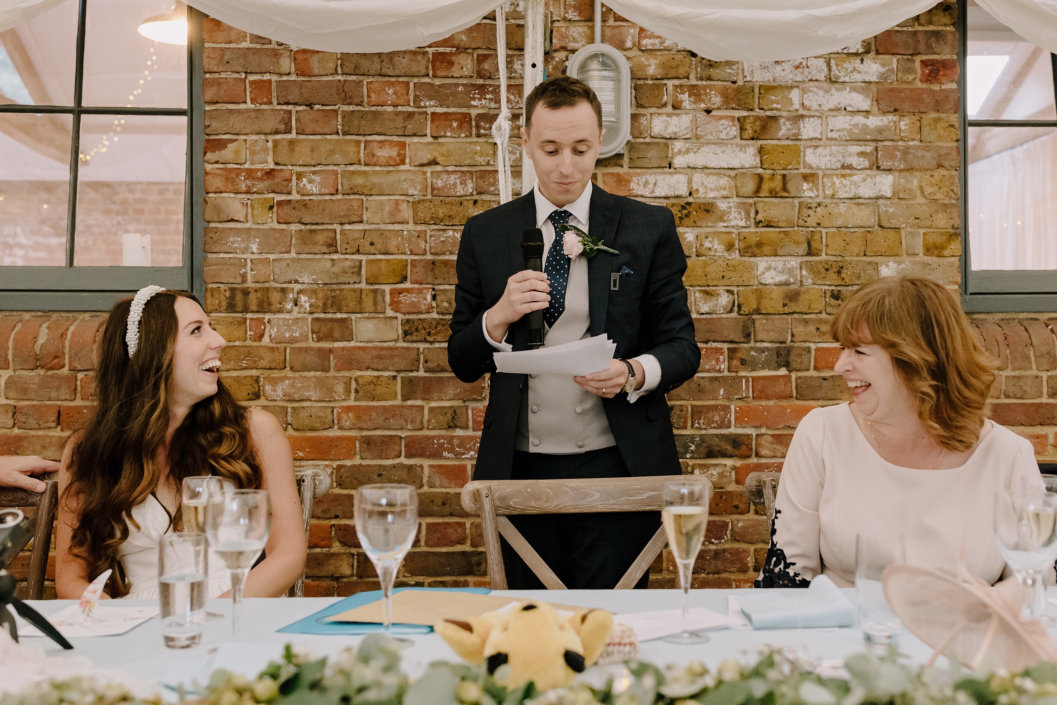 The groom making his wedding day speech with his mum and bride laughing either side