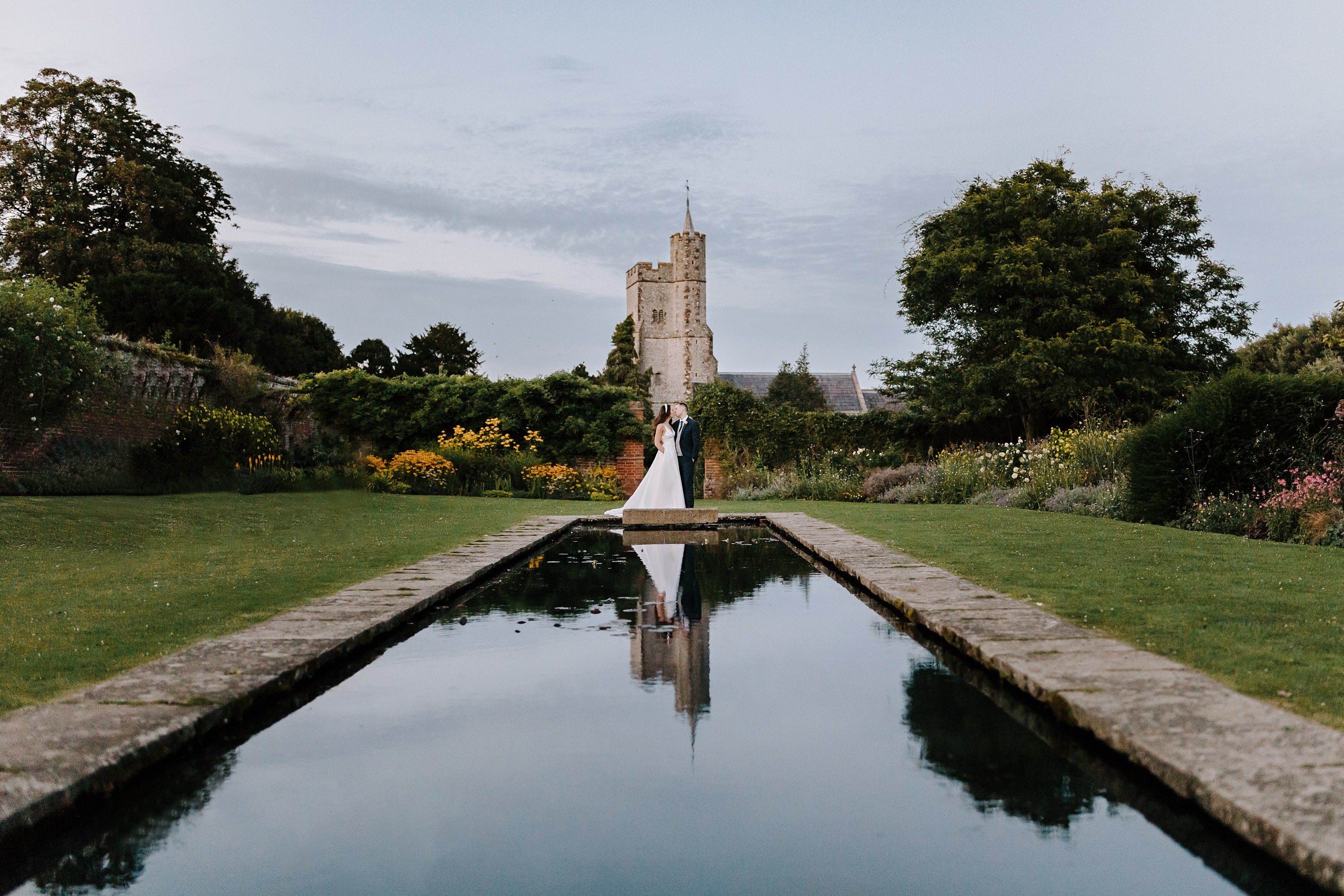 The bride and groom reflected in the ornamental pond in the walled garden at Goodnestone Park at dusk.