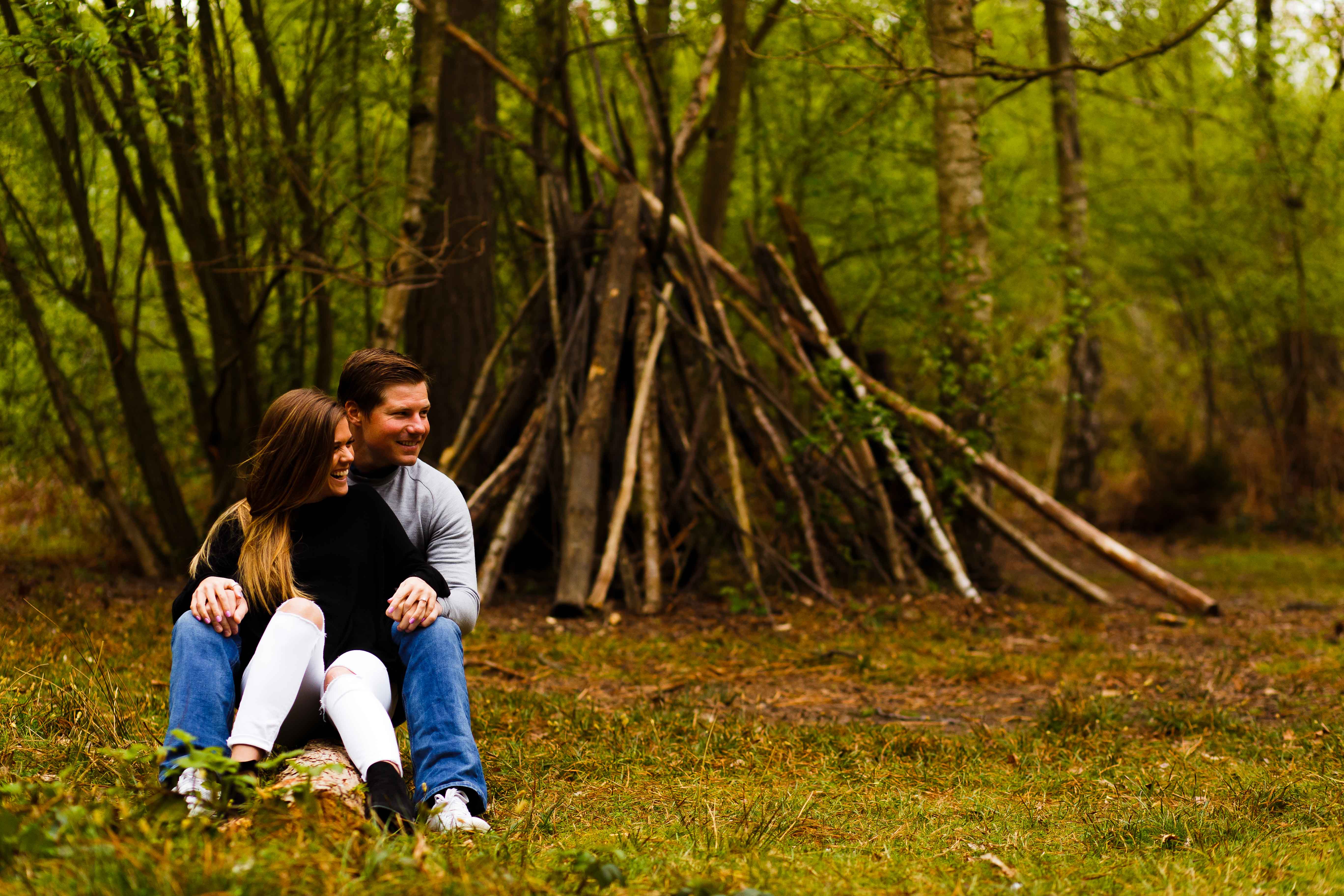 Couple hugging as they seat in the woods during the engagement photos