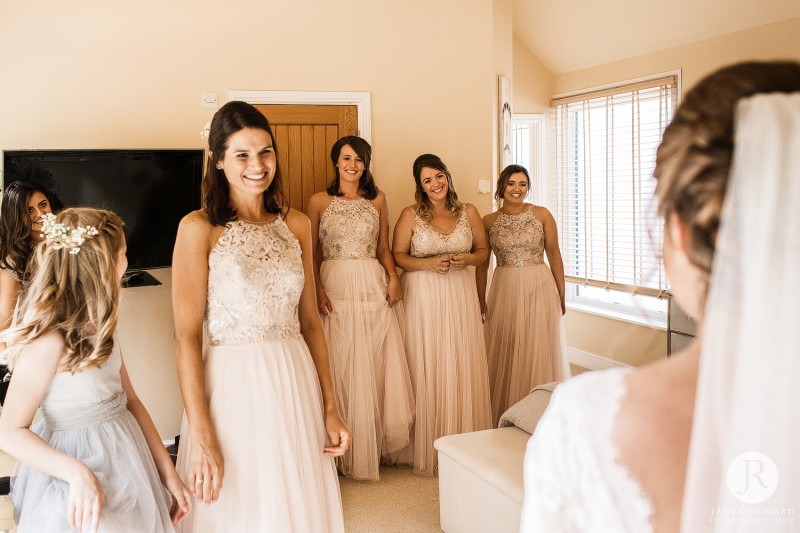 bridesmaids smilling as they see the bride in her dress
